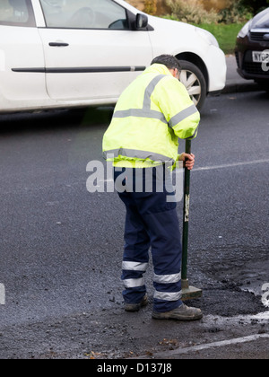 Autorità locale di riparazione su strada uomo facendo una riparazione temporanea per una buca su una strada molto trafficata Foto Stock