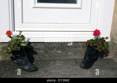 Vecchio stivali neri usati come vasi di fiori su un gradino della porta in bagno, Somerset England Regno Unito Foto Stock