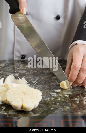 Lo Chef vestita di nero e di bianco uniforme per affettare spicchio di aglio Foto Stock