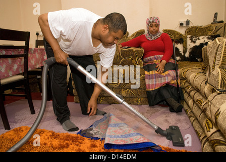 Il marito che si prende cura di sua moglie disabili (seduto, amputazione della gamba) a casa facendo il hoovering, Londra, Regno Unito. Modello rilasciato l'immagine. Foto Stock