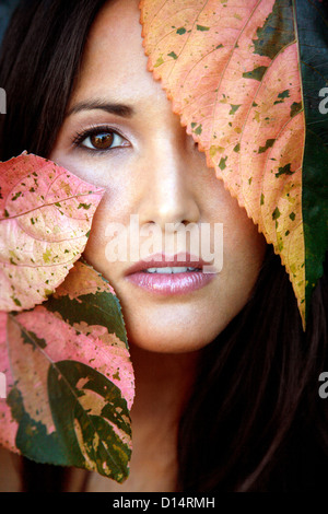 Hawaii, Oahu, primo piano della giovane femmina di bellezza Headshot con foglie colorate accanto al suo volto. Foto Stock