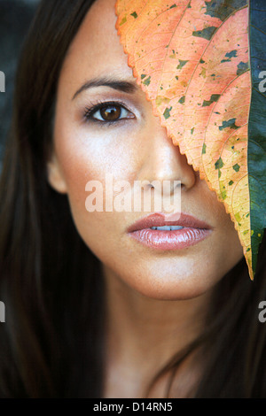 Hawaii, Oahu, primo piano della giovane femmina di bellezza Headshot con foglie colorate accanto al suo volto. Foto Stock