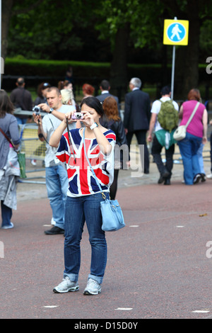 Turista donna che indossa la T-shirt Union Jack che scatta una foto al Pall Mall dopo Trooping the Colour, Londra, Inghilterra Foto Stock