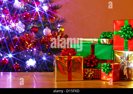 Gift Wrapped regali di Natale su una tavola e un decorate albero dietro con fata luci accese, Foto Stock