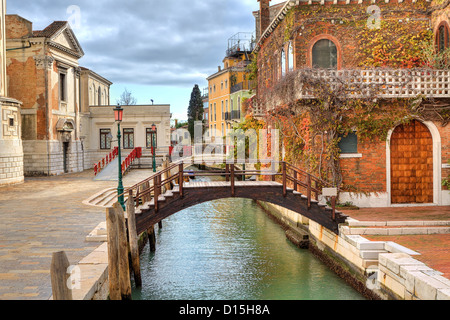 Piccolo ponte in legno sul canale stretto e tradizionale veneziano casa di mattoni ricoperti di edera a Venezia, Italia. Foto Stock