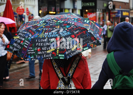 In cerca di riparo dalla pioggia con ombrello coloratissimo (Canterbury UK) Foto Stock