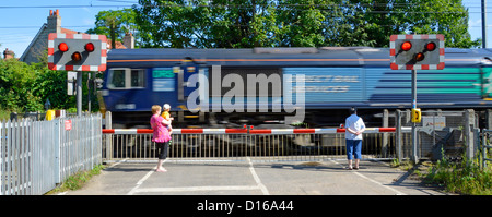 I binari ferroviari rosso lampeggiante spia livello di segno attraversando i cancelli di barriera stradale del paese guardando il treno motion blur Margaretting Essex England Regno Unito Foto Stock