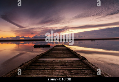 Il sole tramonta su un vecchio pontile in legno sulla flotta lagunare nel Dorset con nuvole riflettono ancora l'acqua. Foto Stock