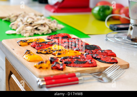 Fette di rosso e giallo peperoni arrosto o peperoni su un tagliere di legno. Foto Stock