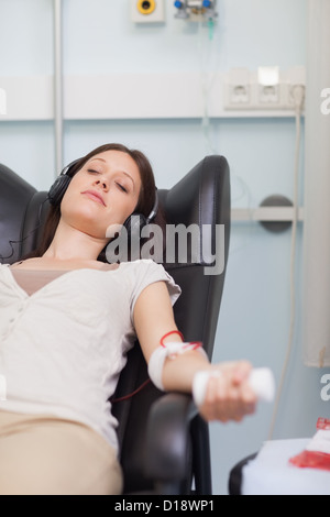 Paziente femmina di ascoltare musica mentre dà il suo sangue in un ospedale Foto Stock