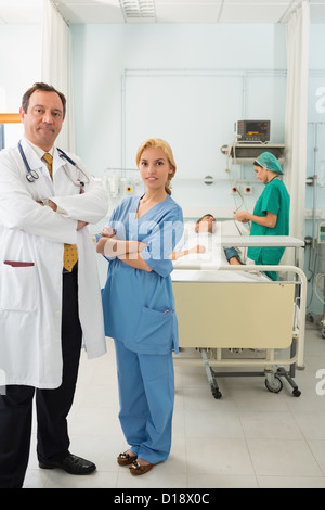 Sorridente medico e infermiere in piedi in una stanza di ospedale mentre la piega le braccia Foto Stock