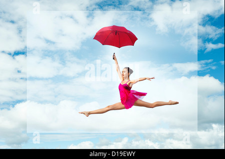 Ballerina con ombrellone, saltando contro il cielo nuvoloso Foto Stock