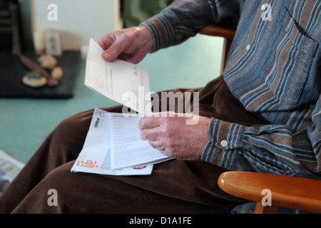 Dettaglio degli anziani uomo seduto in poltrona la lettura / azienda bill o lettera ufficiale, Suffolk, Inghilterra, Regno Unito Foto Stock