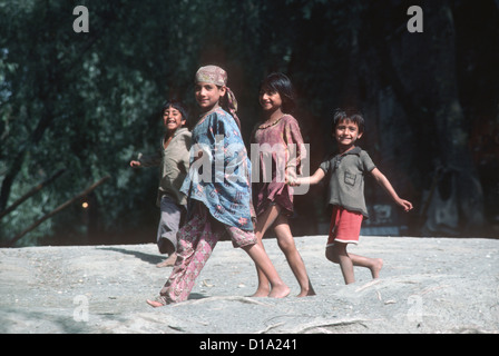 Quattro Kashmir felici i bambini corrono lungo le rive del fiume Jhelum e sorriso per la fotocamera Foto Stock