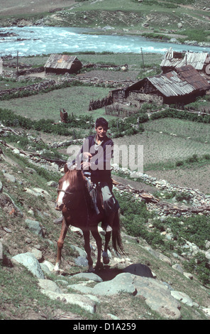 Il Kashmir - il giovane cavaliere cavalca ripida collina dal suo villaggio accanto al fiume Sind nei foothills dell'Himalaya. Foto Stock