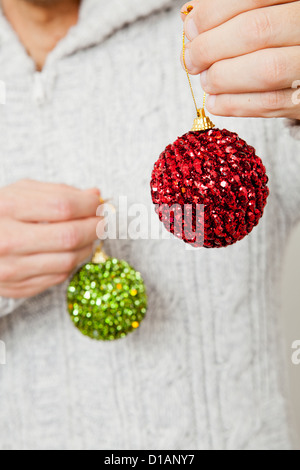 Primo piano del rosso e del verde di Natale baubles appesi da dita Foto Stock