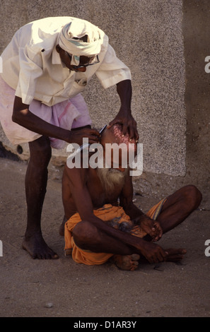 L'uomo la rasatura i suoi capelli sul sentiero. Tamil Nadu India Foto Stock