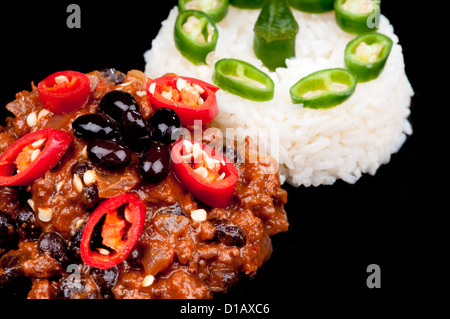 Caldo e peperoncino piccante con carne guarnita con peperoni rossi e riso al pepe verde. Su nero Foto Stock