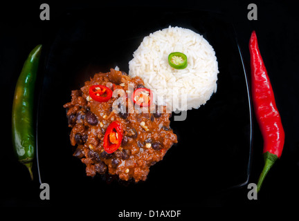 Caldo e peperoncino piccante con carne con peperoni rossi e verdi invece di un coltello e forchetta e riso. Su di una piastra di nero su nero. Foto Stock