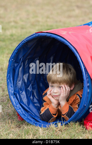 Ragazzo giovane giacente in un tunnel di agilità Foto Stock