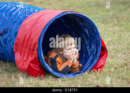 Ragazzo giovane giacente in un tunnel di agilità Foto Stock