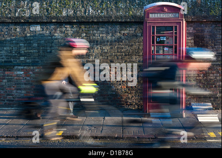 I ciclisti con motion blur passando un tradizionale telefono rosso box Regent Street Cambridge Regno Unito Foto Stock