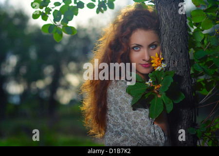 Bella ragazza appoggiata contro un albero guardando la telecamera Foto Stock