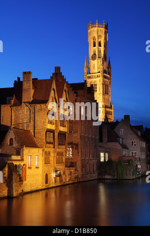 Illuminata del XIII secolo torre campanaria di notte lungo il canale Djiver a Bruges, Belgio Foto Stock