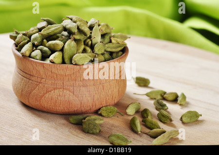 Green i semi di cardamomo in ciotola di legno sul bordo di taglio Foto Stock