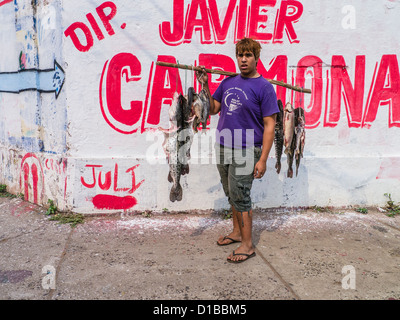 Un giovane uomo sorge su un angolo di strada con il pesce per la vendita, appeso a stringhe da un palo che egli saldi sulla sua spalla. Foto Stock