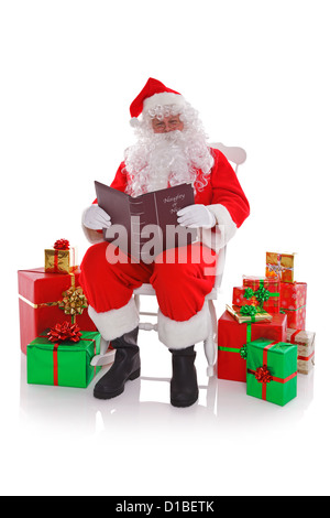 Babbo Natale seduto su una sedia a dondolo circondato da regalo si presenta come egli legge il cattivo o Nizza elenco Foto Stock