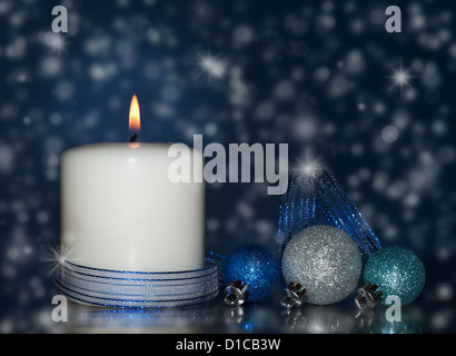 Trasognata Natale Immagine di una candela bianca con la masterizzazione e baubles bokeh nevicata su sfondo blu Foto Stock