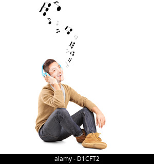 Un giovane ragazzo su un pavimento ascoltando musica su cuffie e note intorno a lui isolato su sfondo bianco Foto Stock