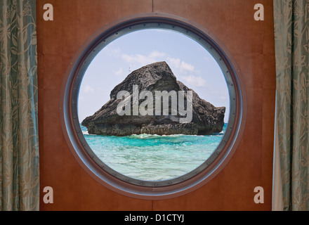 Una grande roccia nell'oceano atlantico nelle acque costiere di Bermuda visto attraverso gli oblò di una nave da crociera. Foto Stock