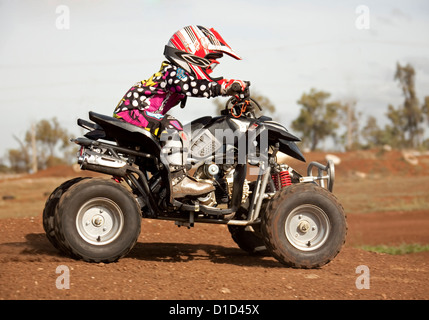 Bambino - di età compresa tra i quattro - su quad bike indossando un abbigliamento protettivo e cavalcare su sterrato Foto Stock