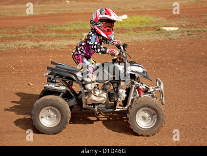 Bambino - di età compresa tra i quattro - su quad bike indossando un abbigliamento protettivo e cavalcare su sterrato Foto Stock