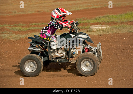 Bambino - di età compresa tra i quattro - su quad bike indossando un abbigliamento protettivo e cavalcare su sterrato Foto Stock