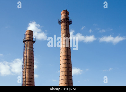 Due mattoni vecchi camini con aste parafulmine contro un cielo blu Foto Stock