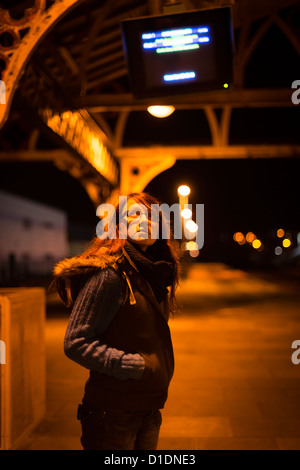 Una giovane donna ragazza adolescente persona sola su una deserta stazione ferroviaria piattaforma in attesa di un treno di notte, REGNO UNITO Foto Stock