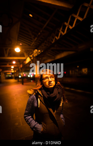 Una giovane donna ragazza adolescente persona sola su una deserta stazione ferroviaria piattaforma in attesa di un treno di notte, REGNO UNITO Foto Stock