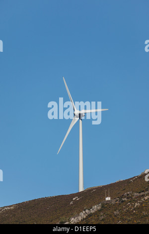 Il vento di generazione di energia elettrica a turbina di mulino a vento stagliano contro il cielo blu sulla cima di una collina Foto Stock