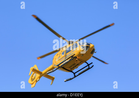 Giallo Scottish Air Ambulance Service elicottero volando overhead da una missione di soccorso visto da sotto contro un cielo blu. Sutherland Scotland Regno Unito Foto Stock