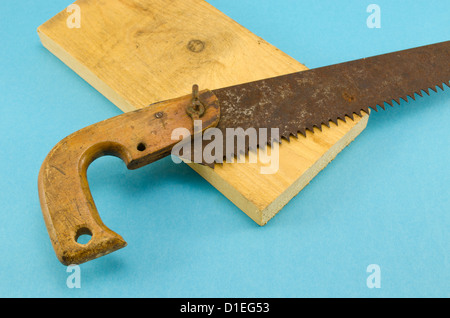 Retrò rusty trasversale sega a mano handsaw utensile e parte della tavola di legno su sfondo blu Foto Stock