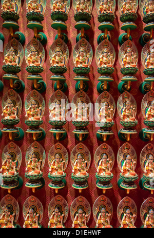 Molte piccole statue buddiste su fiori di loto con parete rossa sullo sfondo. Il fuoco selettivo sulla parte anteriore. Foto Stock