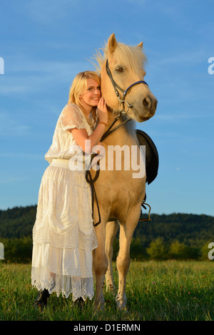 Donna sorridente in abito bianco con cavalli sul prato Foto Stock