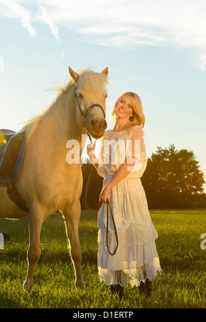 Donna sorridente in abito bianco con cavalli sul prato Foto Stock