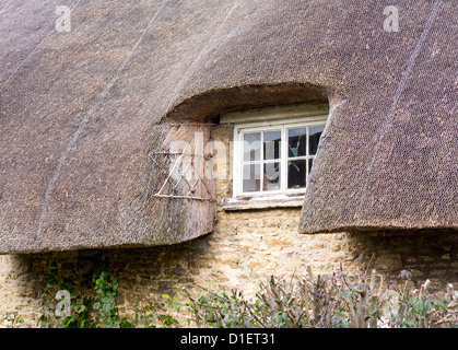 Dipinto di bianco di finestra in legno sotto il tetto di paglia di rurale cottage Foto Stock