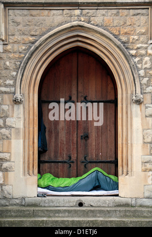 Un uomo dorme in un sacco a pelo in una chiesa porta a Mayfair, London, Regno Unito. Foto Stock