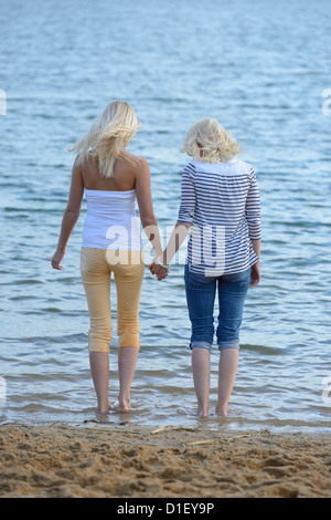 Due giovani donne bionda in piedi mano nella mano a lago balneare Foto Stock