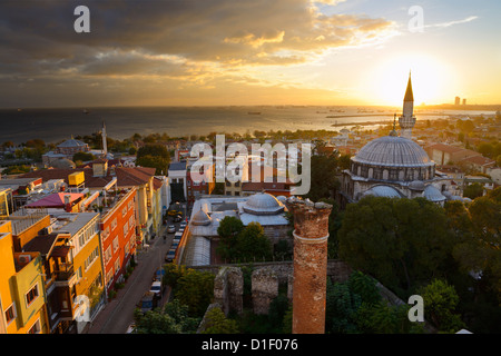 Sole che tramonta dietro la Sokollu Mehmet Pascià minareto della moschea con bagliore dorato sulle case e il Mare di Marmara Istanbul Turchia Foto Stock